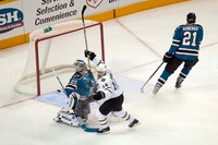 A hockey player fights the goalie for the puck near the net as a defenseman skates away